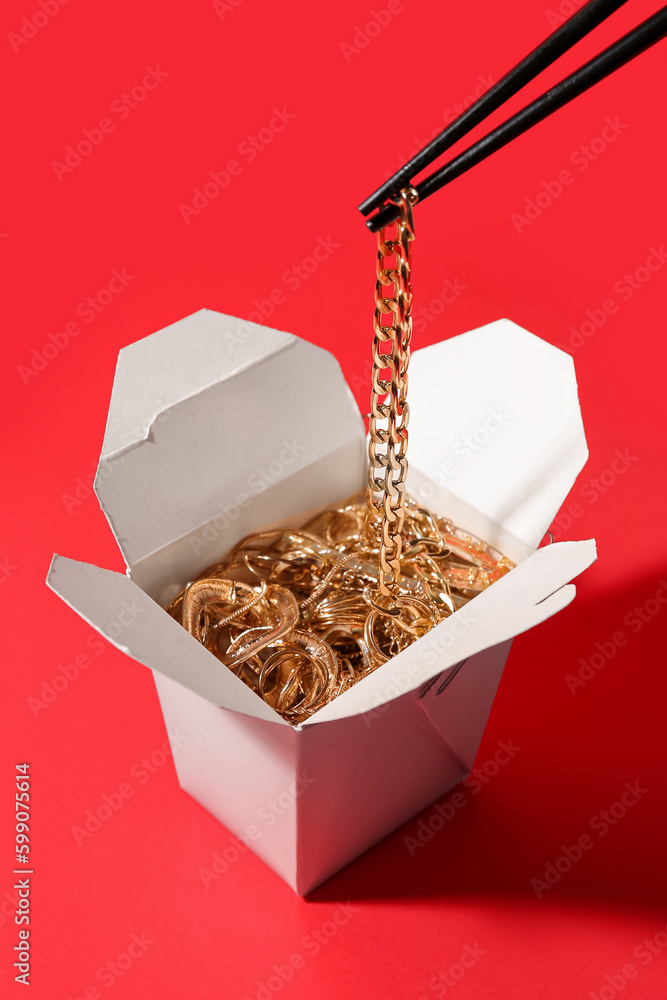 Chopsticks with golden jewelry in box on red background