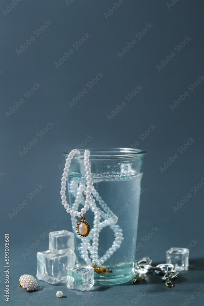 Glass of water with stylish jewelry and ice cubes on grey background