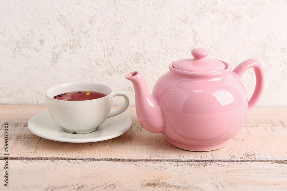 Ceramic teapot with cup of fruit tea on white wooden table