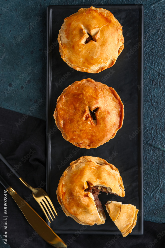 Board with tasty meat pot pies on dark background