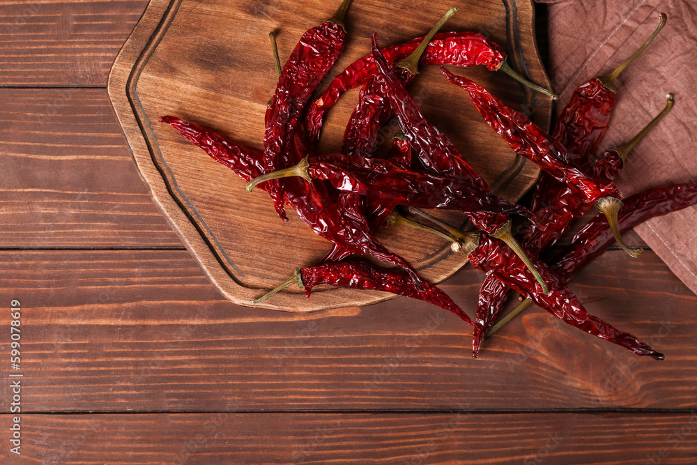 Board with dry hot chili peppers on brown wooden background