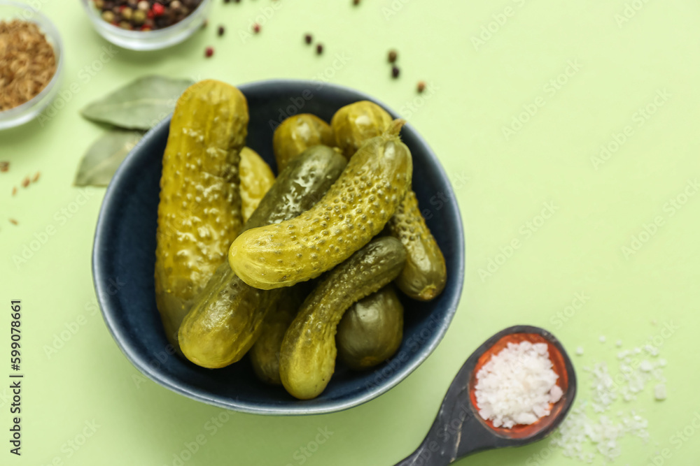 Bowl of tasty canned cucumbers with spices on pale green background