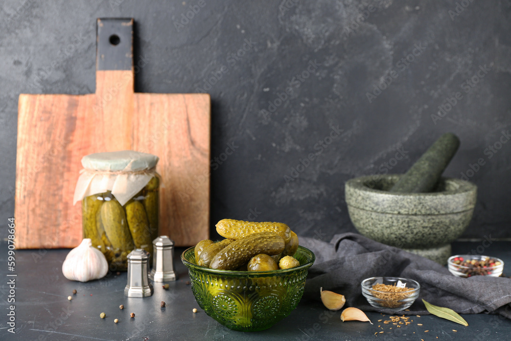 Jar and bowl with tasty canned cucumbers on black table