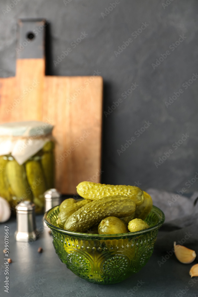 Jar and bowl with tasty canned cucumbers on black table