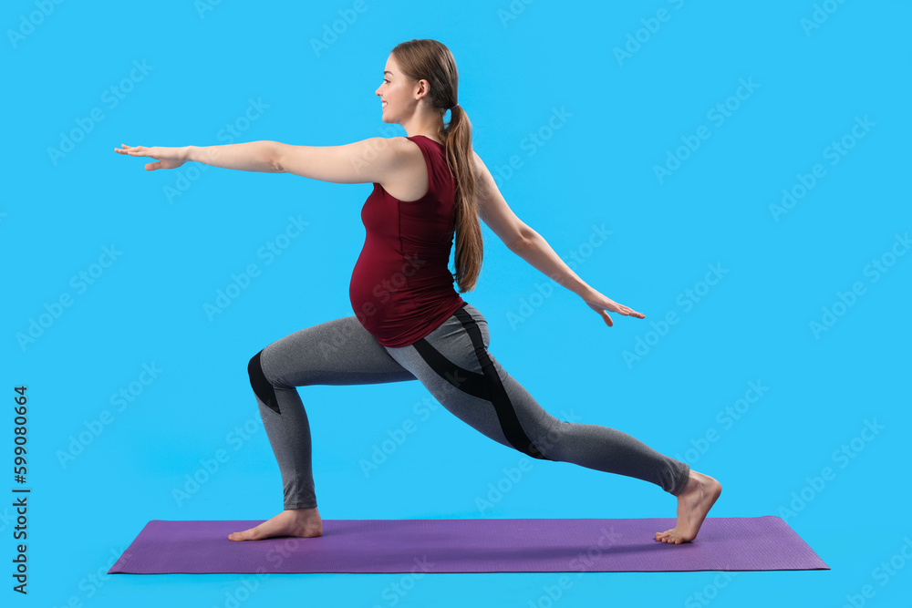 Pregnant young woman doing yoga on blue background