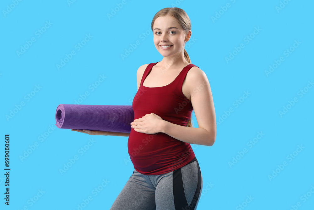 Pregnant young woman with yoga mat on blue background