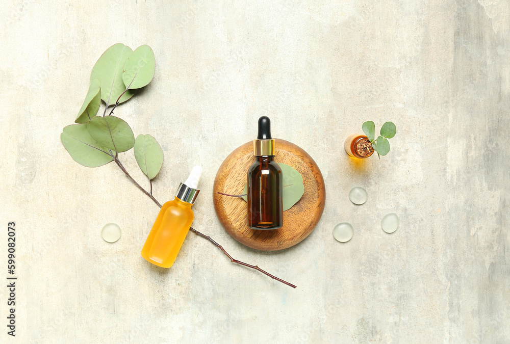 Cosmetic oil bottles with wooden stand and eucalyptus branch on textured background