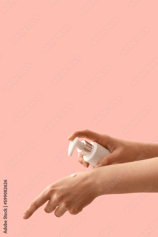 Hands of woman applying cosmetic cream against pink background