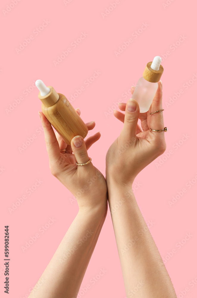 Hands holding cosmetic products on pink background