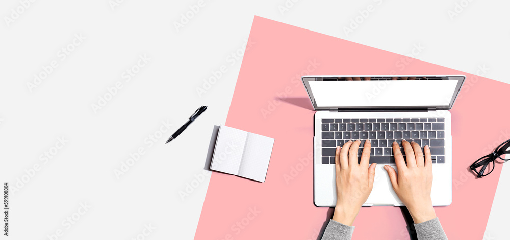 Person using a laptop computer with a notebook and eyeglasses