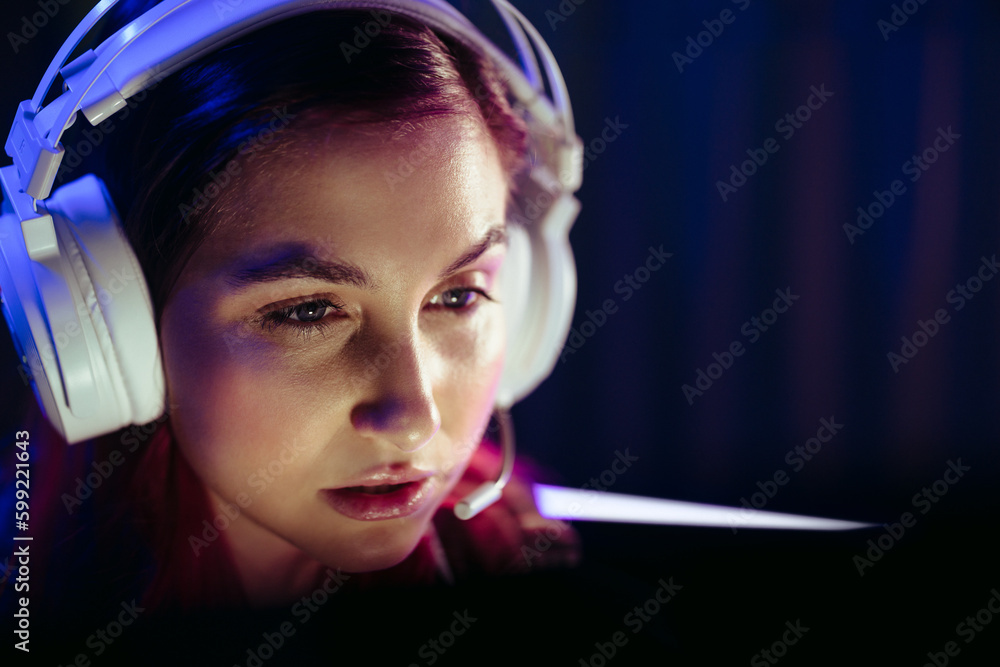 Young female gamer playing a video game at night, wearing headphones