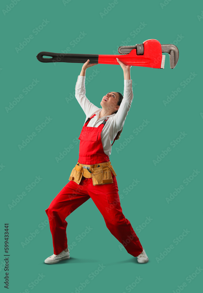 Worried female plumber with big pipe wrench on green background