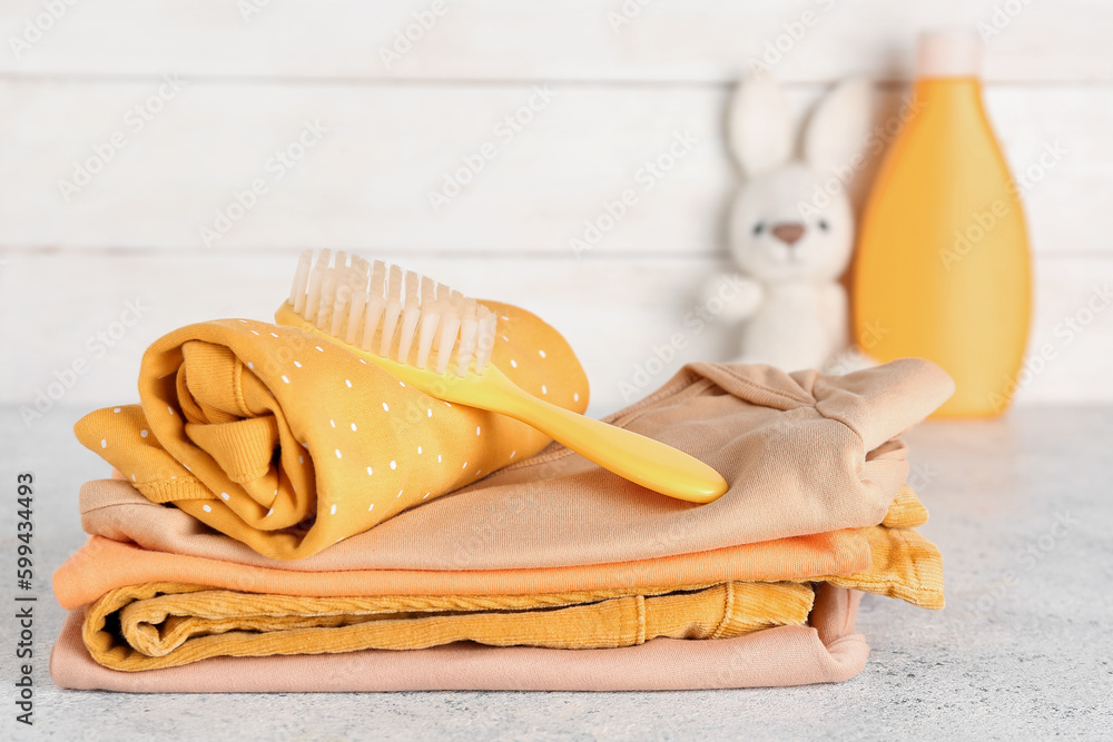 Stack of baby clothes and hair brush on light table