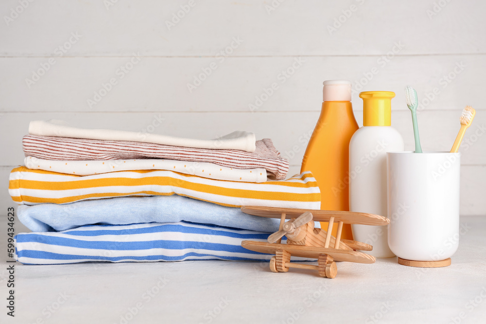 Stack of baby clothes, toothbrushes, cosmetics and wooden toy on light table