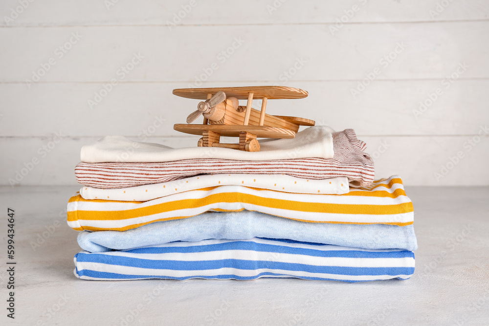 Stack of baby clothes and wooden toy on light table