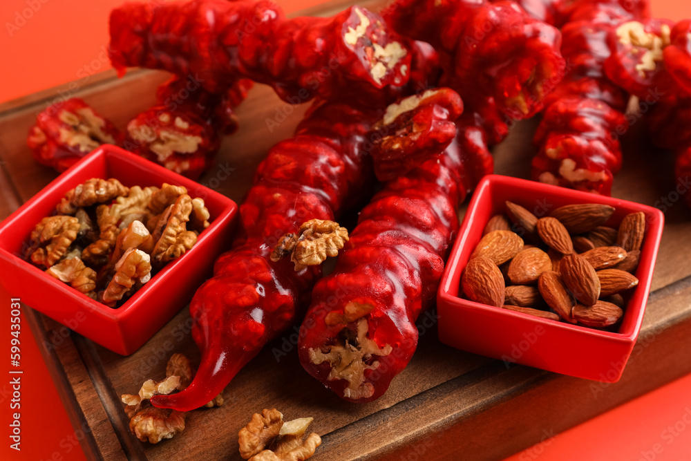 Wooden board with delicious churchkhela and nuts on color background, closeup