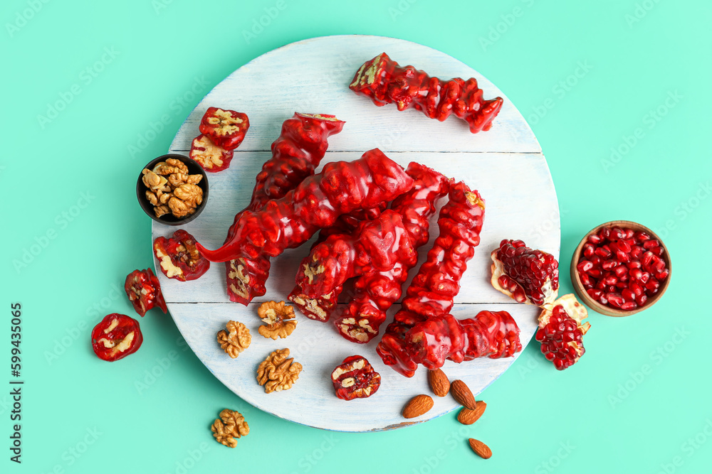 Wooden board with tasty churchkhela, pomegranate and walnuts on color background