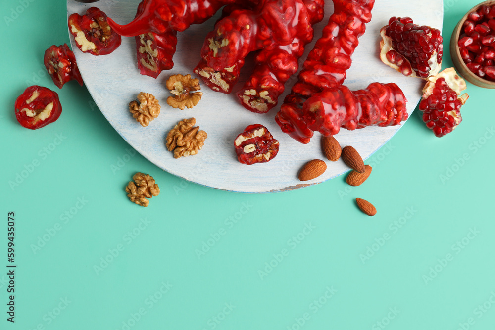 Wooden board with tasty churchkhela, pomegranate and walnuts on color background