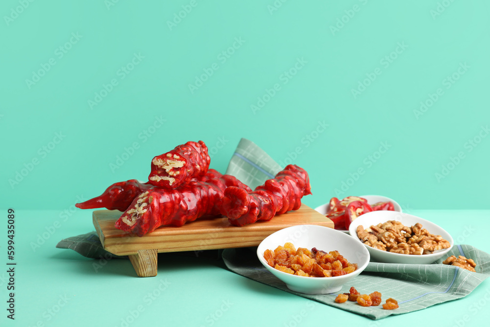 Wooden board with tasty churchkhela, pomegranate and walnuts on color background