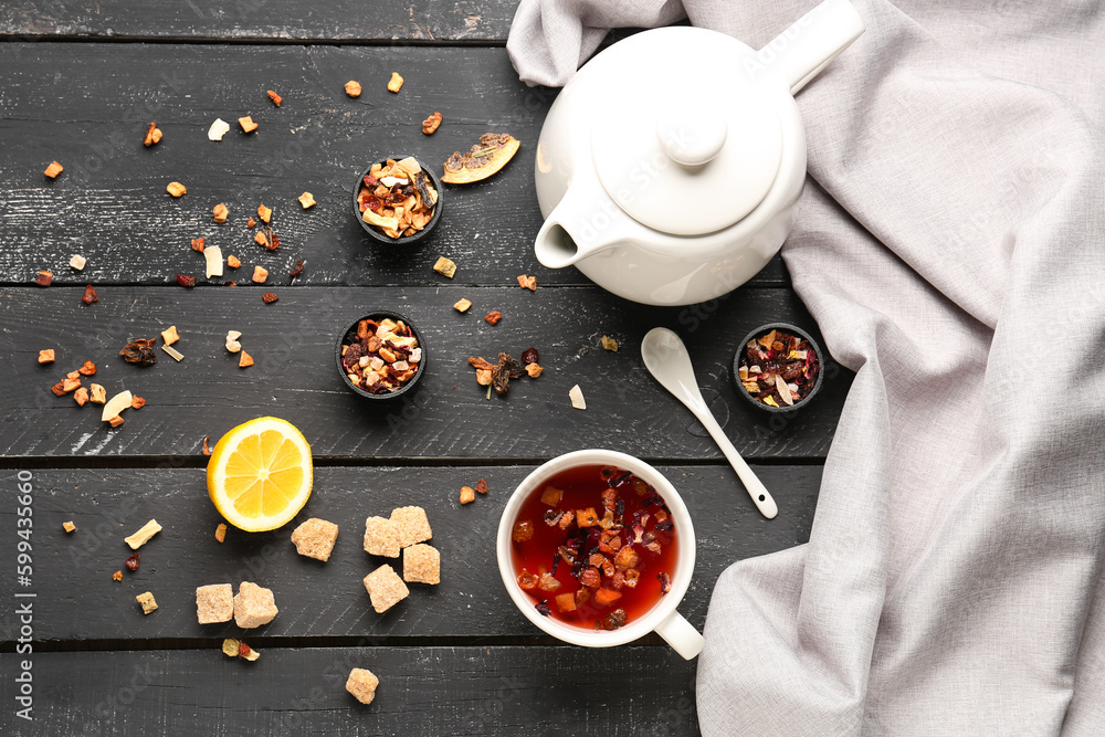 Composition with cup of tea, teapot and scattered dried fruits on black wooden table