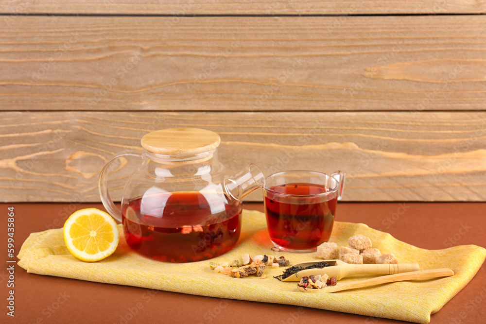 Teapot and glass of fruit tea on brown table near wooden wall