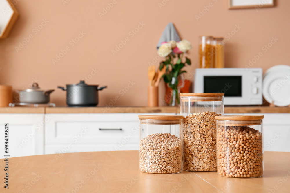 Glass jar with different cereals on wooden table in kitchen