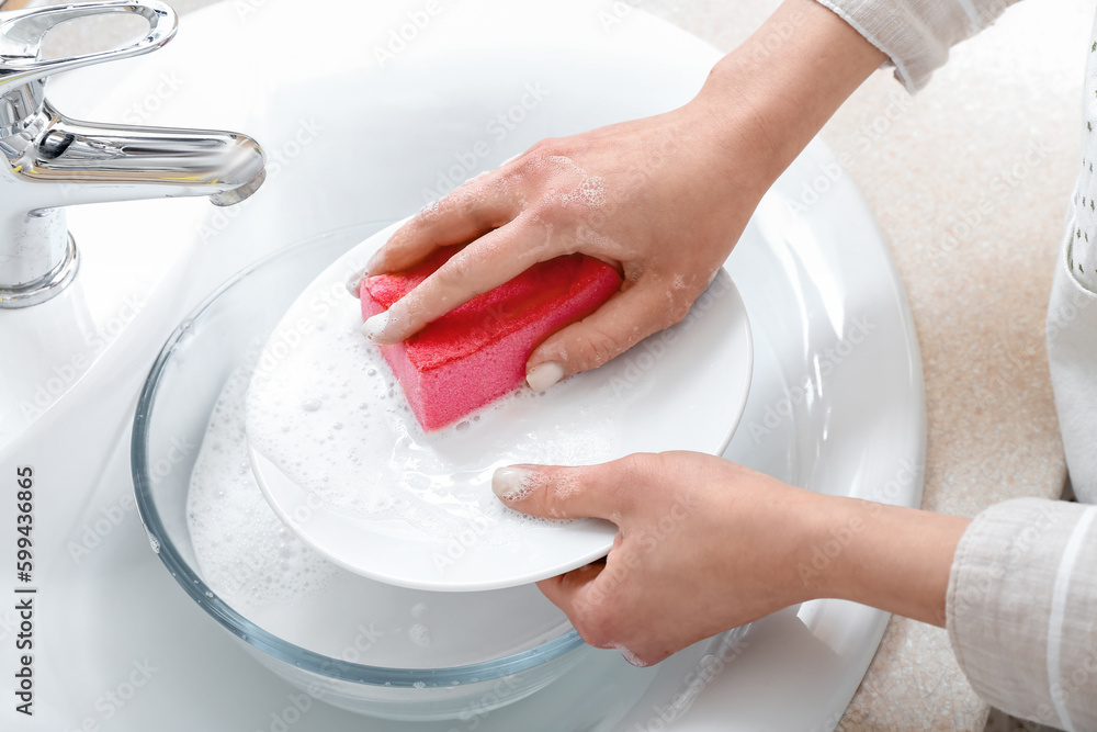 Woman washing plate with sponge in sink, closeup