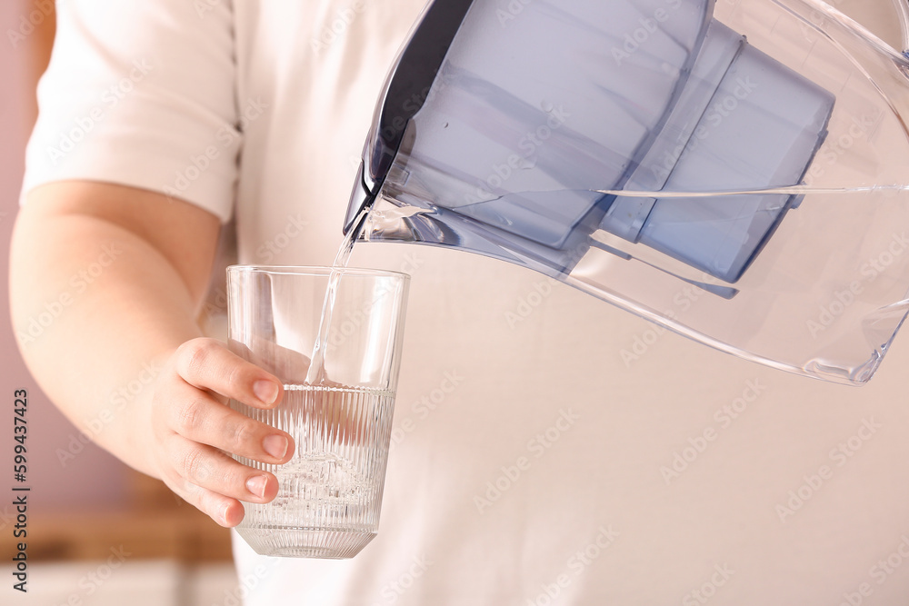 Woman pouring pure water from filter jug into glass