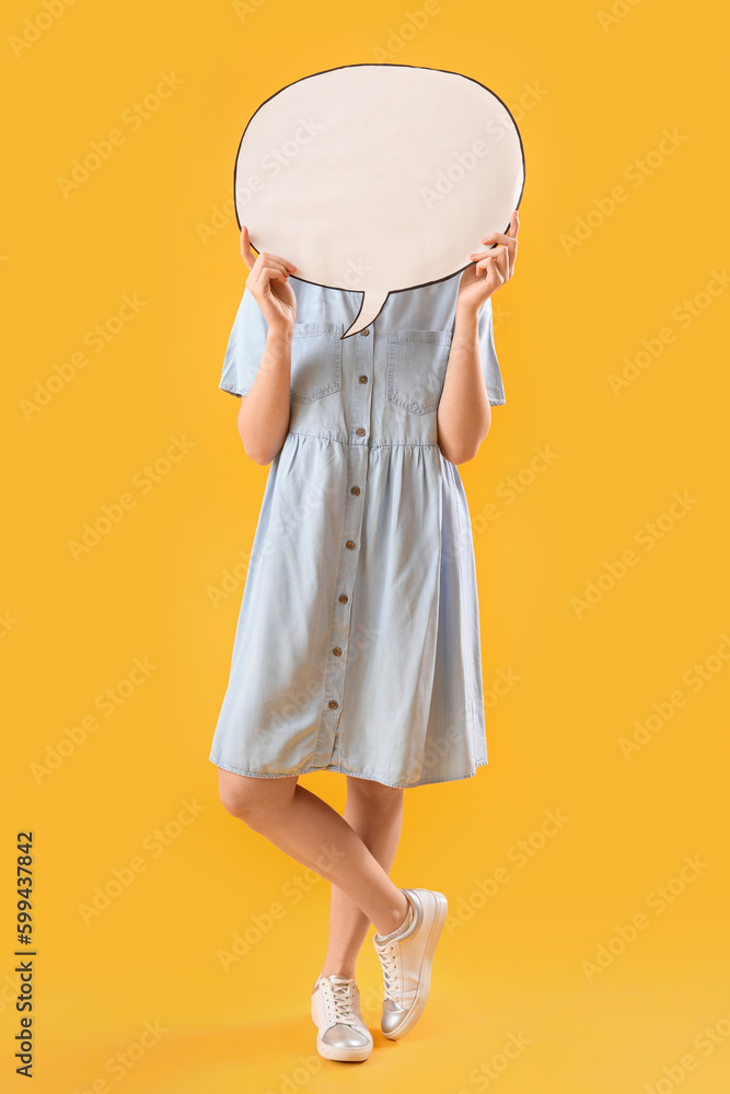 Young woman hiding face behind blank speech bubble on yellow background