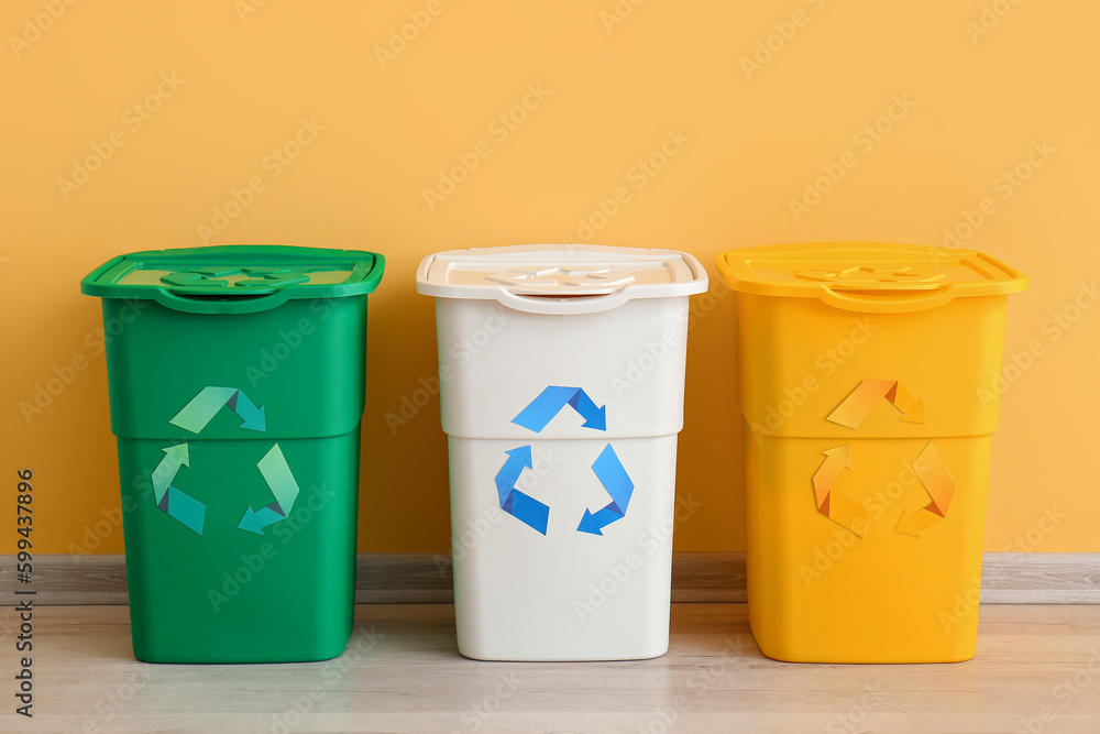 Different garbage bins with recycling symbol near yellow wall