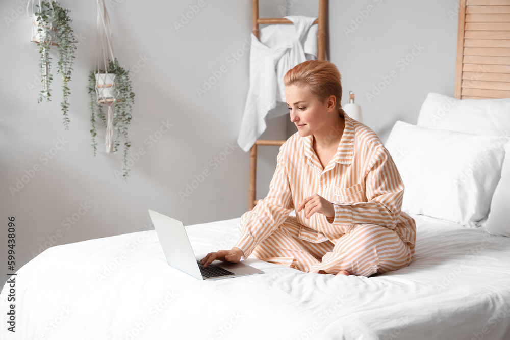 Young woman using laptop on bed in morning