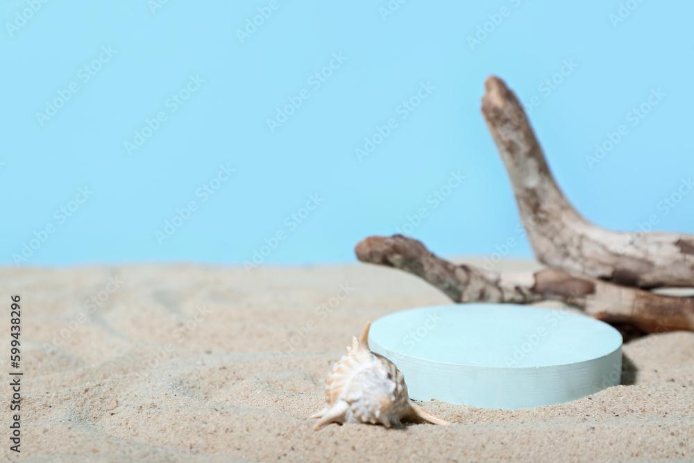 Decorative plaster podium, seashell and tree branch in sand on blue background