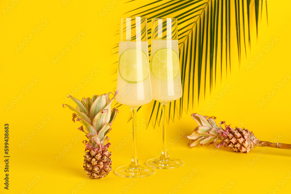 Glasses of cocktail with lime and baby pineapples on yellow background