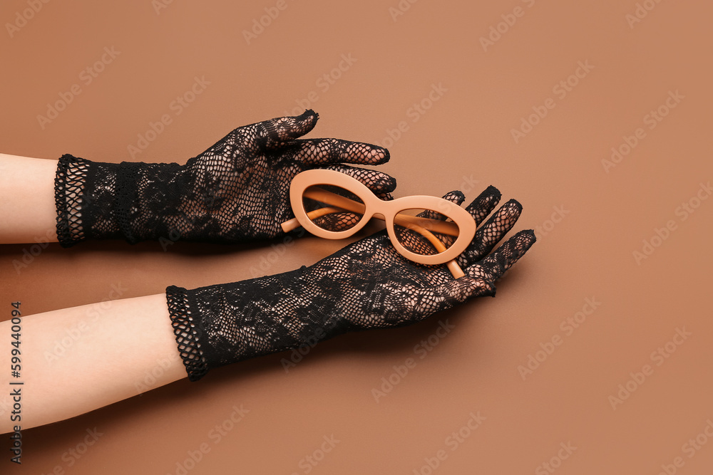 Woman in laced gloves with sunglasses on brown background