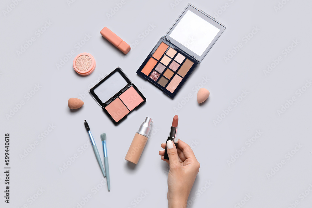 Female hand holding lipstick and different cosmetics on grey background