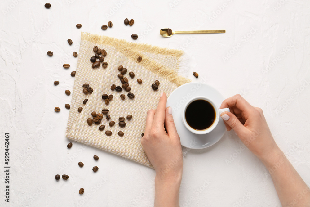 Female hands with cup of coffee and beans on light background