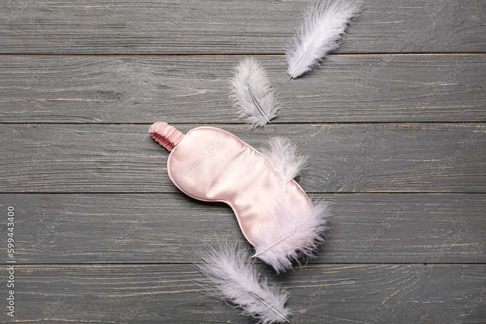 Sleeping masks and feathers on grey wooden background