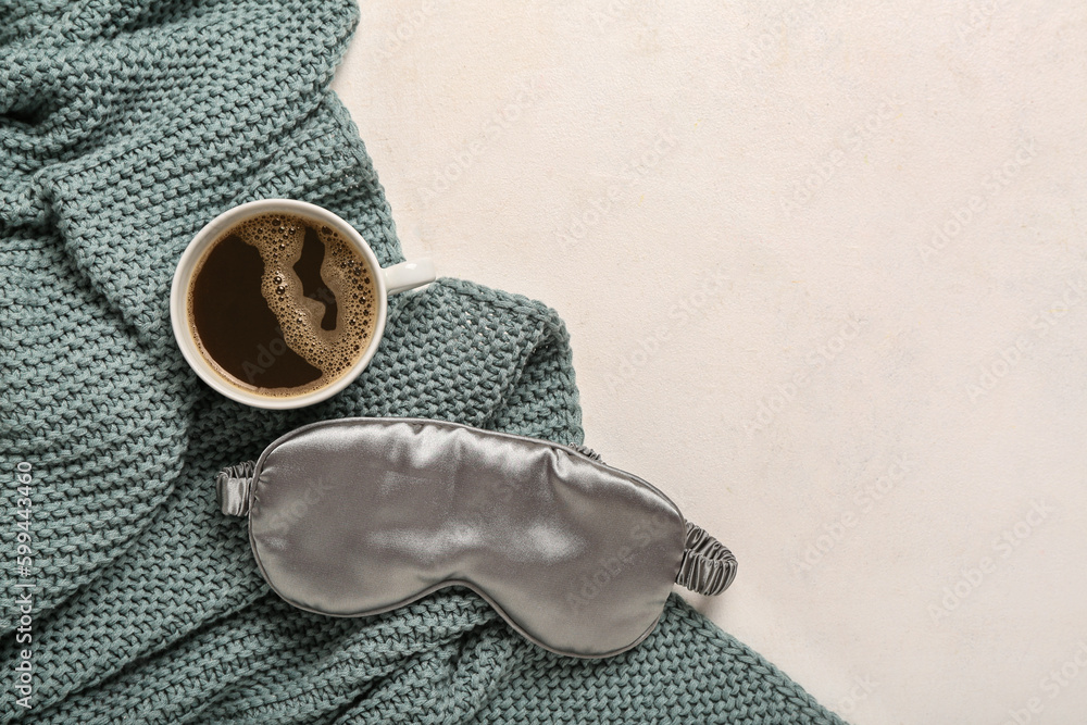 Sleep mask, cup of coffee and knitted blanket on light background