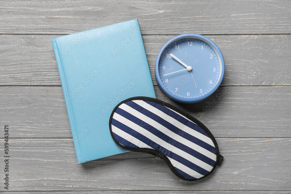 Alarm clock with notebook and sleeping mask on grey wooden background