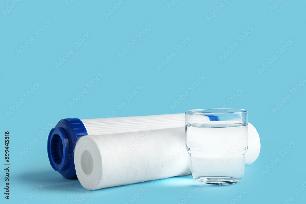 Glass of liquid and water filter cartridges on blue background