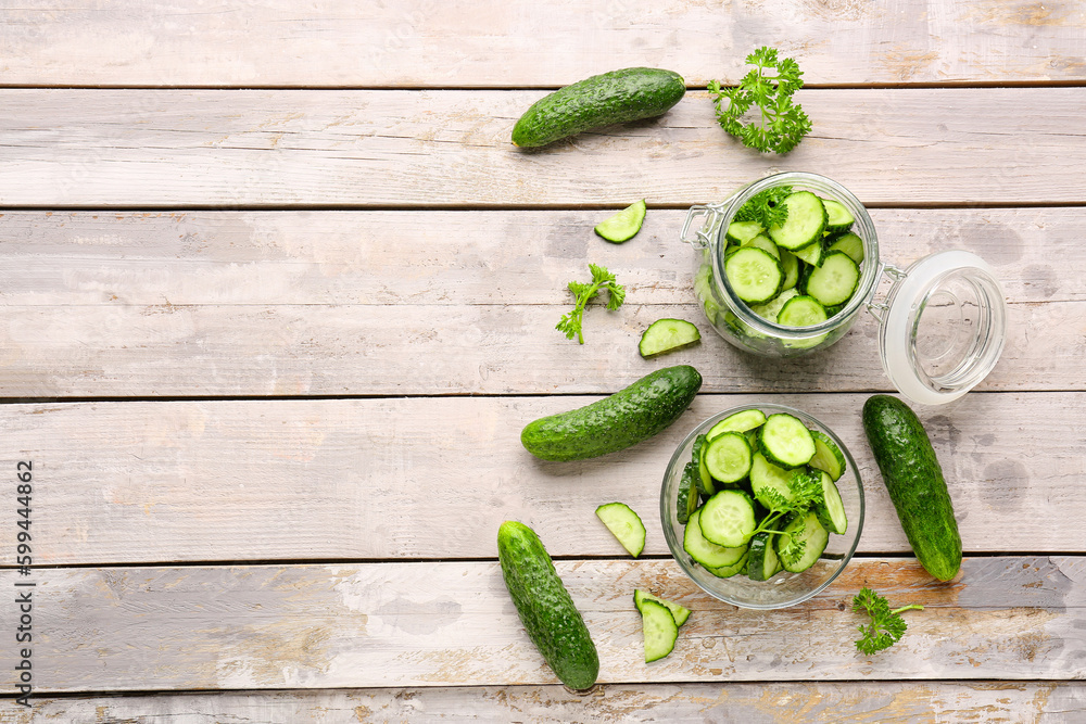 Jar and bowl with fresh cut cucumbers on light wooden background