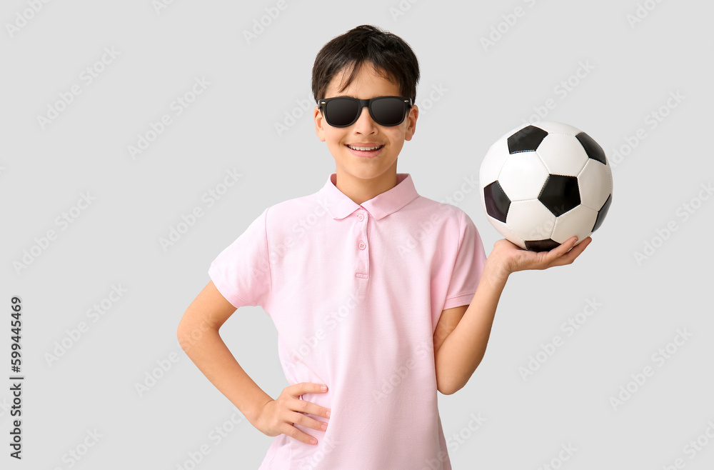 Little boy with soccer ball wearing sunglasses on grey background