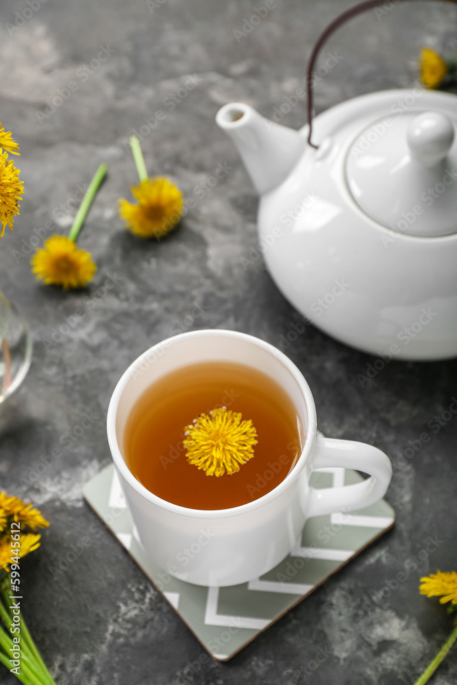 Cup of healthy dandelion tea and teapot on grey background