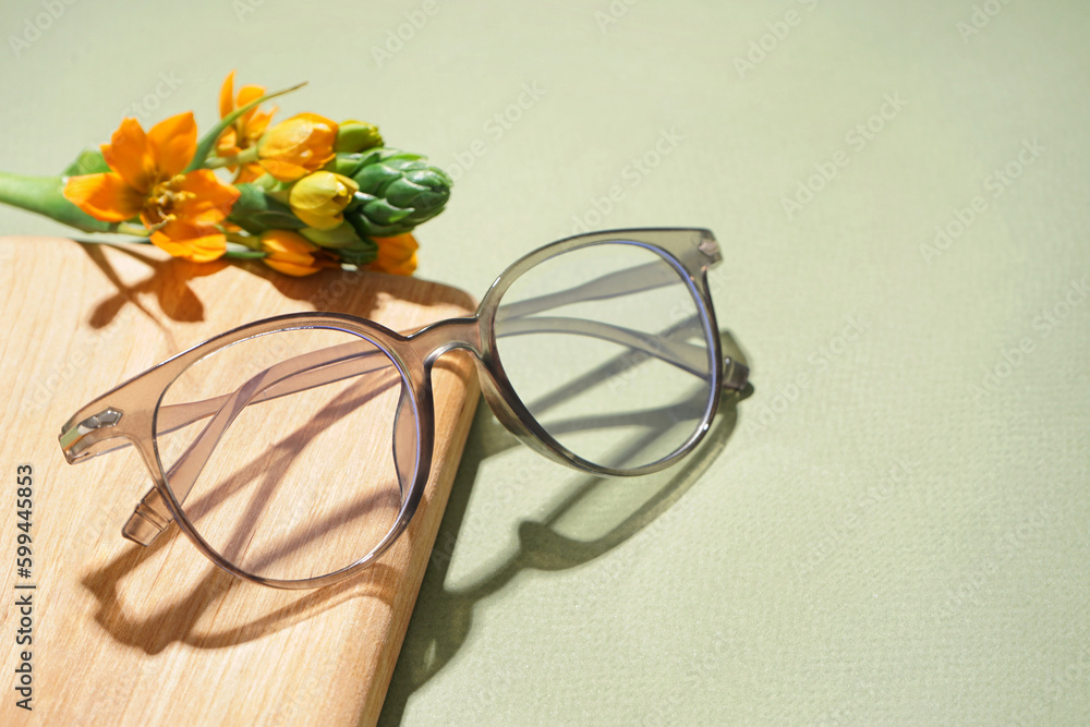 Notebook, flower and eyeglasses on pale green background