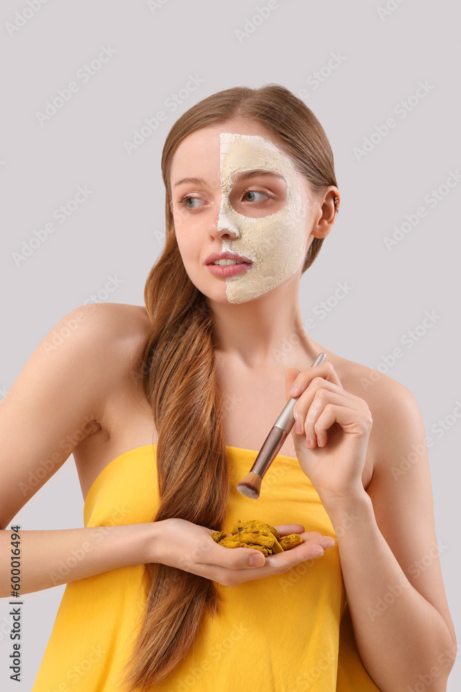 Young woman with applied turmeric mask, brush and roots on grey background