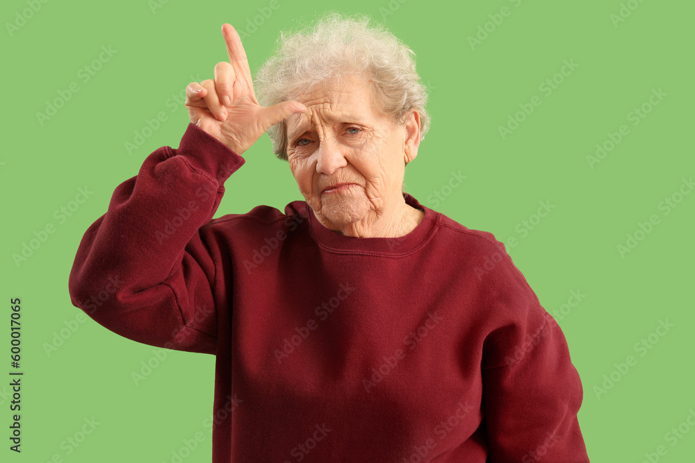 Senior woman showing loser gesture on green background