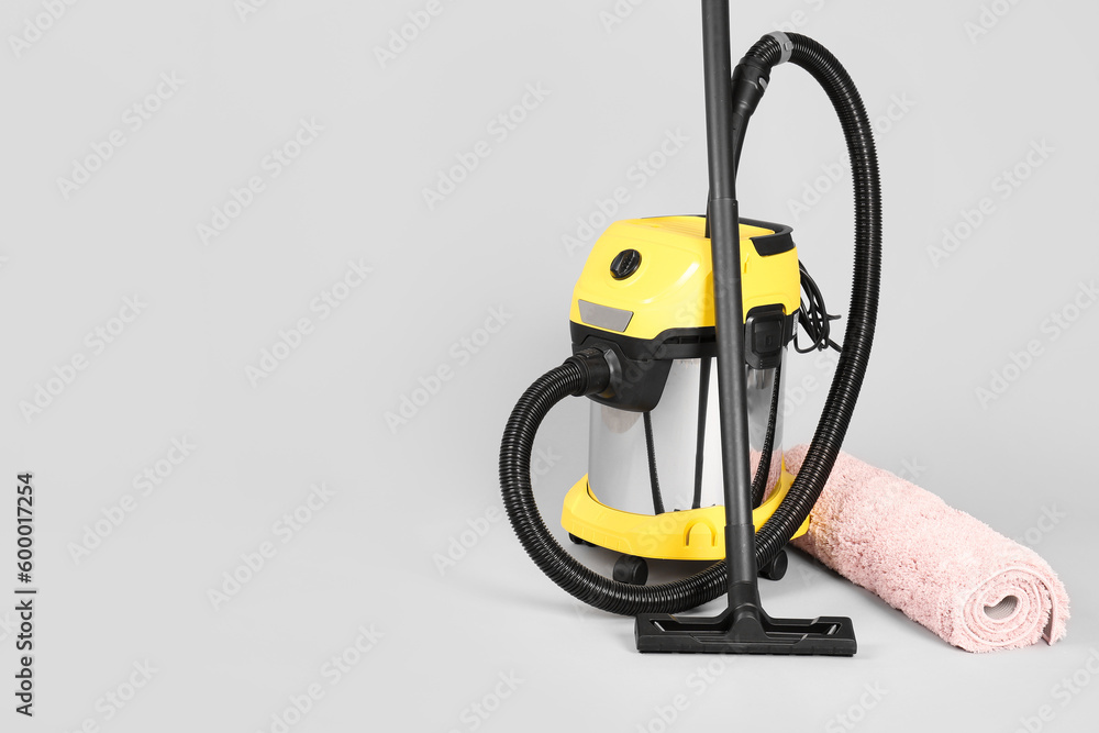 Vacuum cleaner with rolled carpet on grey background