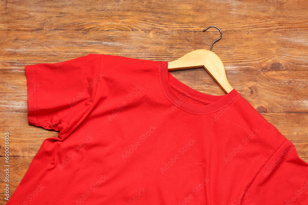 Stylish red t-shirt and hanger on wooden background