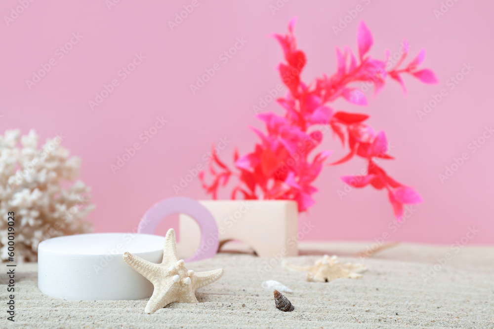 Decorative plaster podiums, coral, seaweed and starfish in sand on pink background