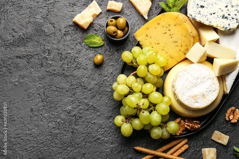 Tray with different types of tasty cheese and grapes on dark background